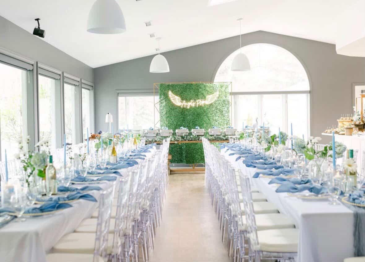 Wedding reception with long blue-and-white tables and a greenery-wall backdrop