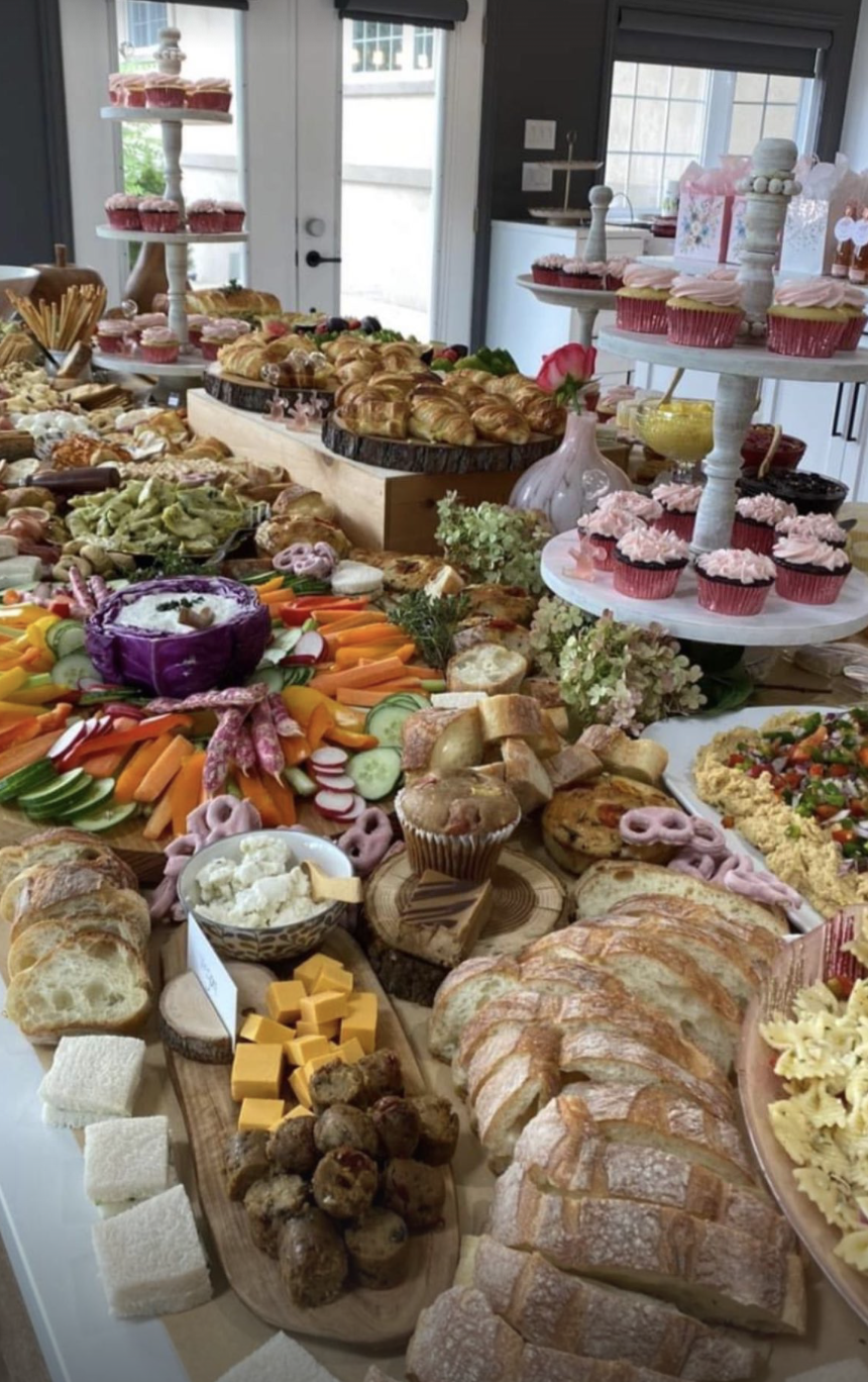 Abundant grazing-table spread with breads, cheeses, charcuterie, and pink cupcakes